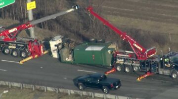 Cranes working to upright garbage truck after rollover on interstate